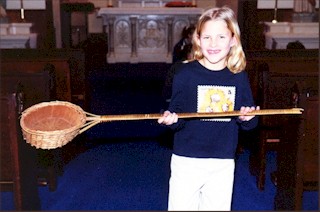 The collection basket, shown here by Rachel Schone, was probably purchased in the early 1930's and has been used each Sunday ever since then. According to the records of the Altar Society, it cost 20 cents.