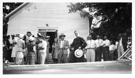 Father Henehan chats with parish members outside the church after Sunday Mass. (Some others identifiable in the photo are Ed Dober (left of Father Henehan), Jim Zillion (to the right, with his arms folded), Bert Kolberer and Leo Jones, to the left of Jim Zillion.) Frank (Pa) Dober is to the far right in the photo. Photo was taken around 1950 (?).